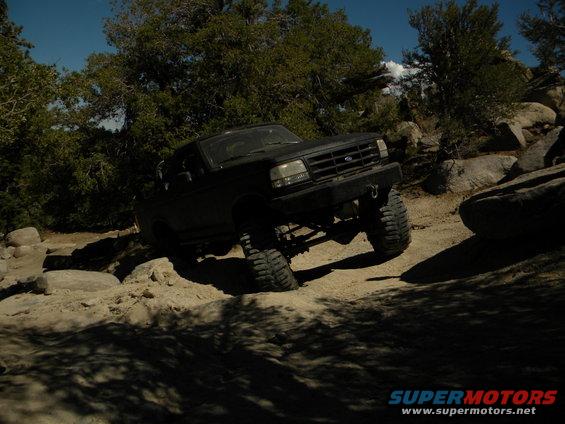 Black 1992 Ford Bronco navigating a rocky off-road trail with large tires and lifted suspension