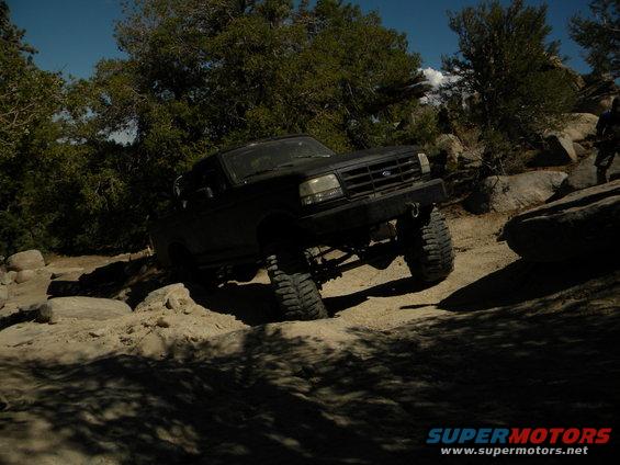 Black SUV with large tires driving over rocks on a dirt trail