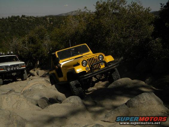 Yellow Jeep CJ-7 navigating a rocky trail, with a white Ford Bronco behind it