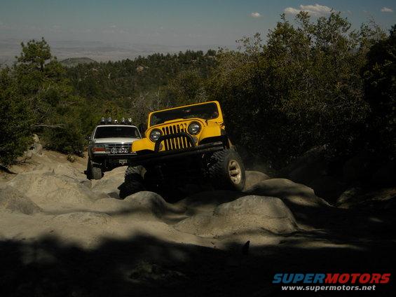White 1992 Ford Bronco and yellow Jeep on rocky trail, front view