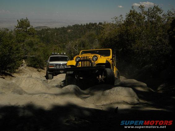 Yellow Jeep and white Ford Bronco driving on a rocky trail