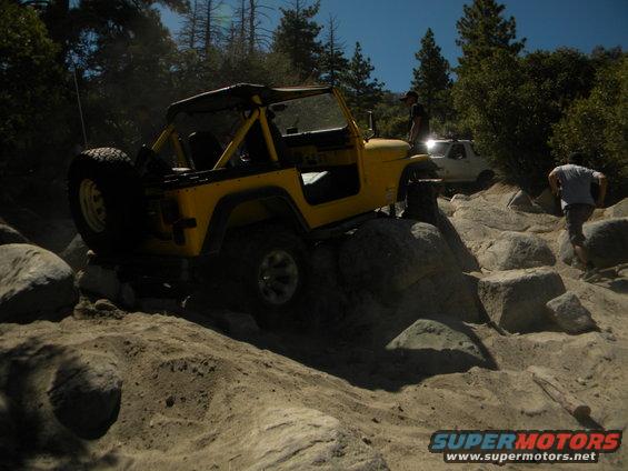 Yellow Jeep Wrangler navigating rocky terrain with a white truck behind it