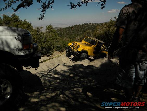 White truck pulling a yellow jeep out of a sandy ditch on a hill