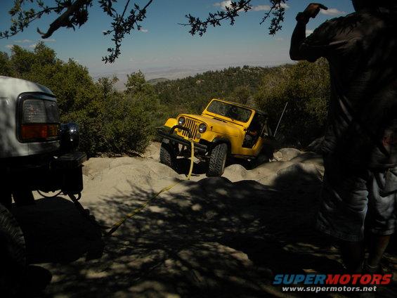 Yellow Jeep Wrangler on rocks, white SUV in foreground