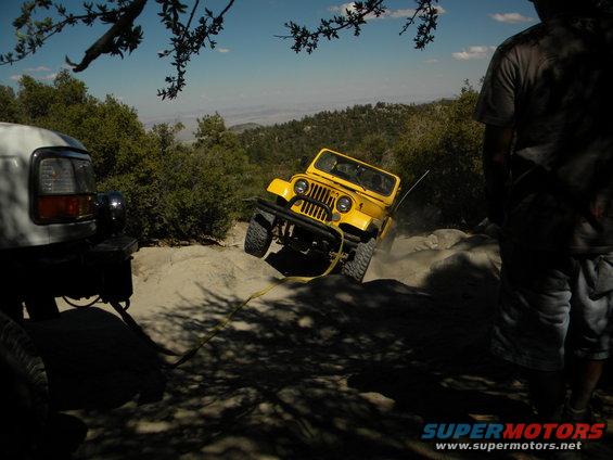 Yellow Jeep CJ-5 on a rocky incline, being pulled by a white SUV. Off-road scene
