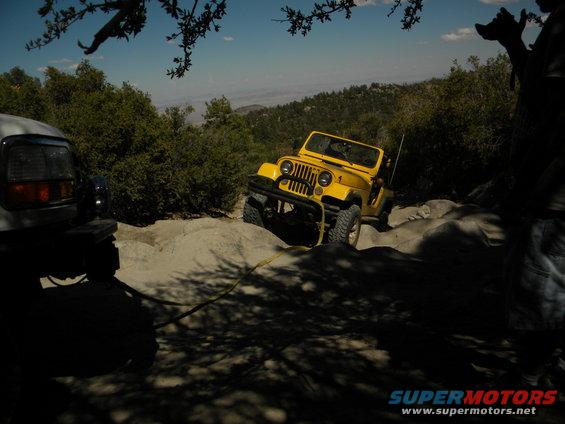 Yellow Jeep CJ-7 on rocky terrain with another vehicle partially visible on the left
