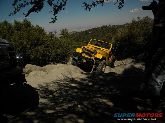 Yellow Jeep Wrangler on a rocky trail, with another vehicle partially visible on the left