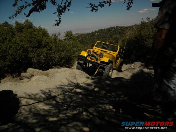 Yellow Jeep Wrangler on rocky terrain with a tow rope