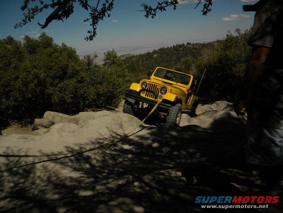 Yellow Jeep Wrangler on rocky terrain with a tow strap attached
