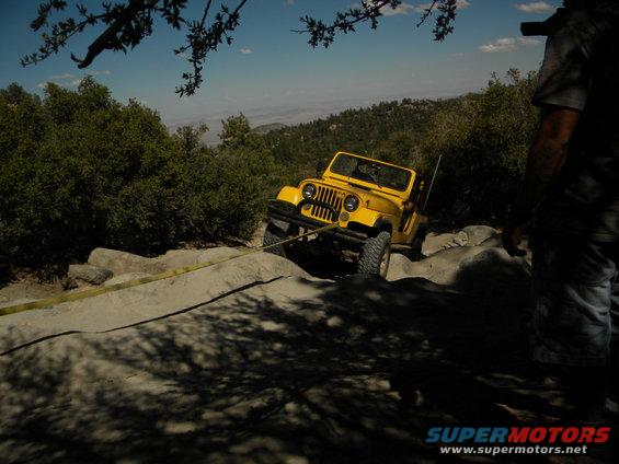 Yellow Jeep CJ being pulled by a yellow strap up a rocky incline