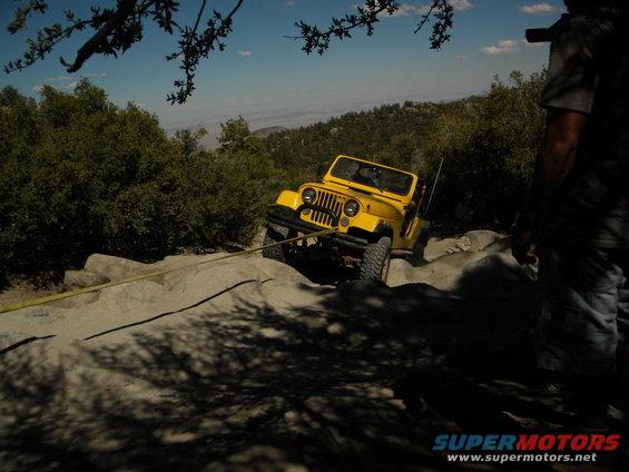 Yellow Jeep Wrangler off-roading on rocky terrain with a tow strap