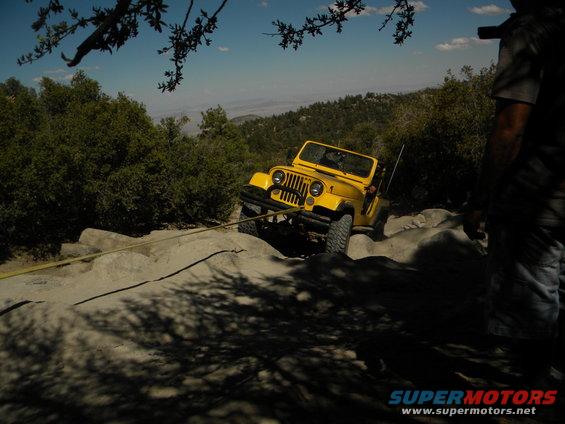Yellow Jeep Wrangler on rocky terrain with a tow rope attached