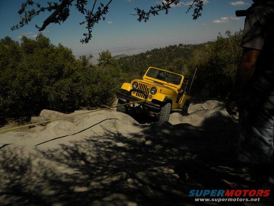 Yellow Jeep Wrangler being pulled by a yellow strap up a rocky incline