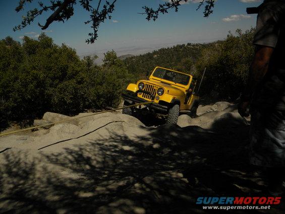 Yellow Jeep Wrangler on rocky terrain, being pulled by a rope. Off-road scene
