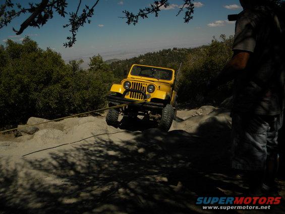 Yellow Jeep being pulled by a rope on a rocky trail