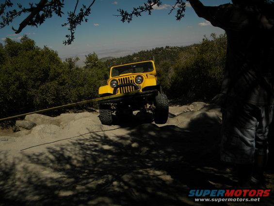 Yellow Jeep CJ on rocky terrain with a tow strap