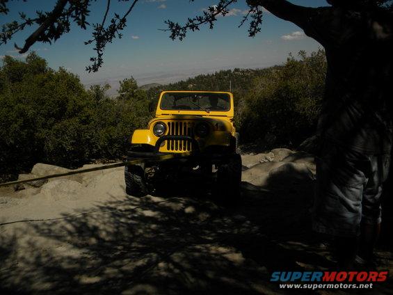 Yellow Jeep with black grille guard parked on a dirt road