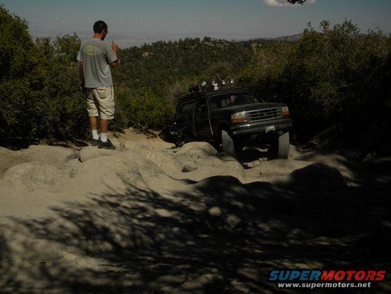 Black Ford Explorer climbing over rocks on a trail. A man stands on rocks watching