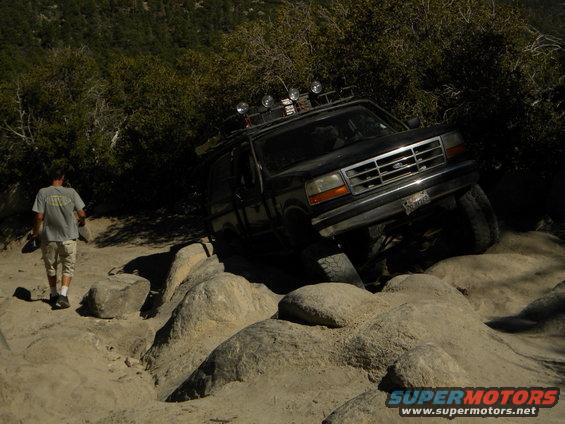 1992 Ford Bronco navigating a rocky trail with a person walking nearby
