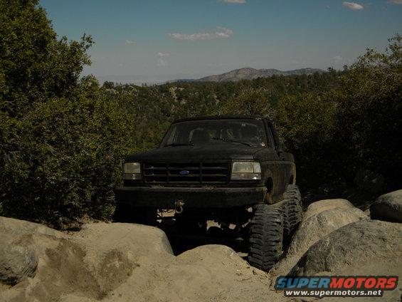 Black Ford pickup truck with large tires navigating rocks on a trail