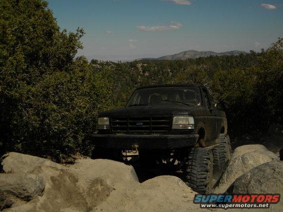 Black 1992 Ford Bronco on a rocky trail with trees and mountains in the background