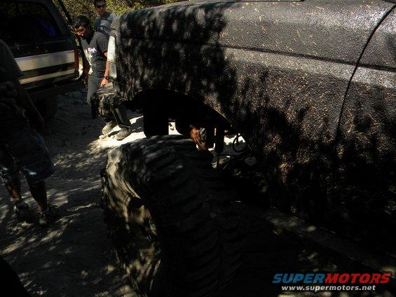 Black 1992 Ford Bronco side view, muddy, with large tires, parked on dirt road