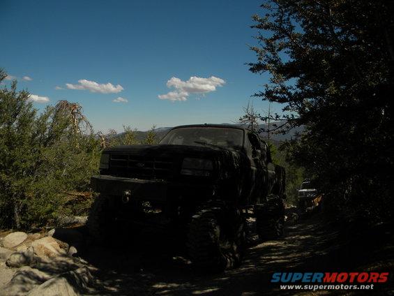 Black pickup truck with large tires on a dirt road, another vehicle visible in the distance