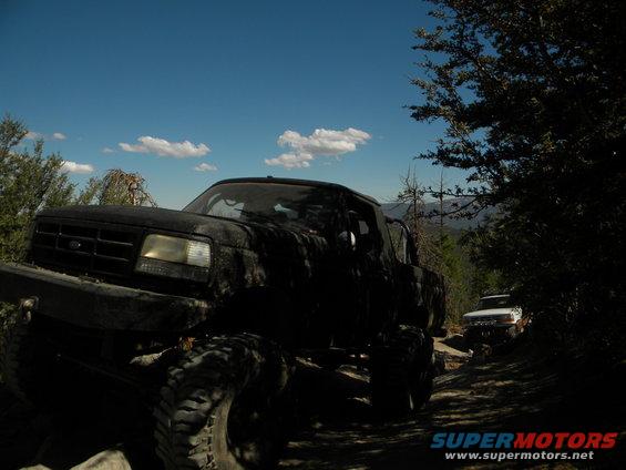 Black lifted pickup truck on dirt road, another white truck behind