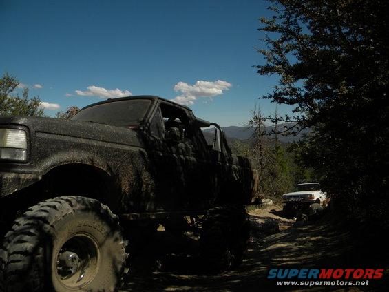 Muddy 1992 Ford Bronco in foreground, white truck on trail behind it
