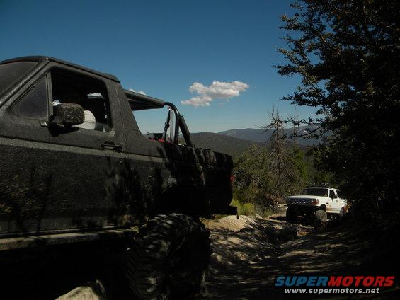 Black 1992 Ford Bronco on a dirt road, side view, with a white Ford truck behind it