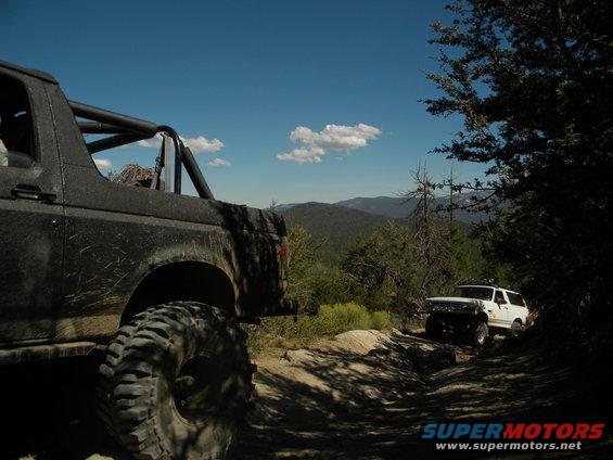 1992 Ford Bronco off-road with roll cage and large tires on a dirt trail