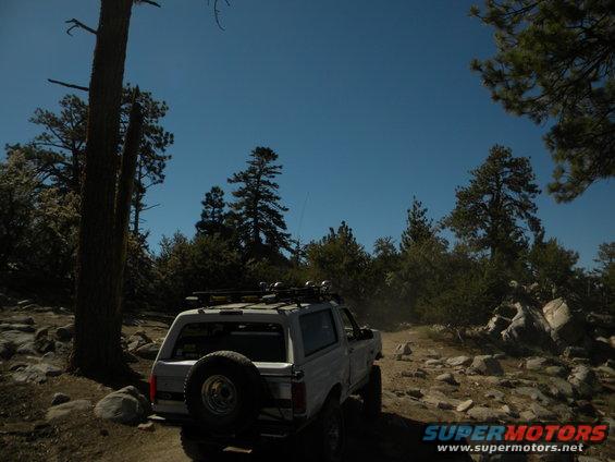 White SUV with spare tire on rear door, roof rack, driving on a rocky dirt road