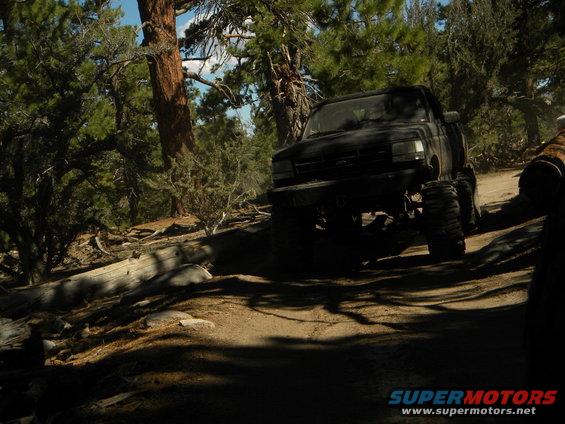 Black 1992 Ford Bronco with large tires driving on a wooded dirt road