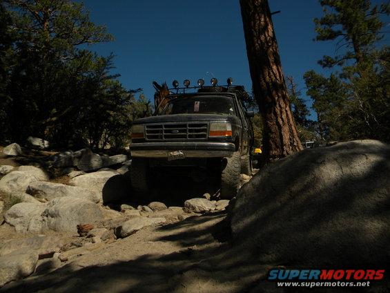 Dark 1992 Ford Bronco on rocky terrain, front view, with roof rack and off-road lights