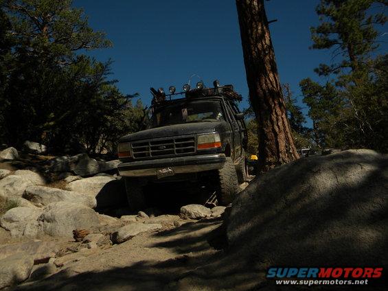 Black 1992 Ford Bronco navigating a rocky trail with a roof rack