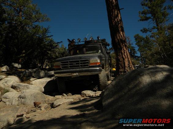 1992 Ford Bronco navigating a rocky trail with trees and blue sky