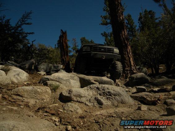 Black 1992 Ford Bronco climbing over large rocks on a wooded trail