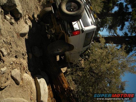 White 1992 Ford Bronco tilted on its side on a rocky, wooded trail