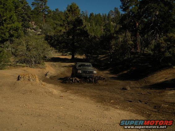 Dark 1992 Ford Bronco driving through mud on a dirt road