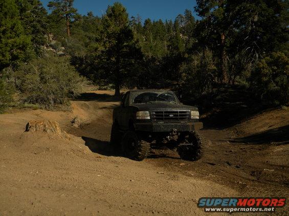 Dark 1992 Ford Bronco on a dirt road, lifted with large tires, front grille visible