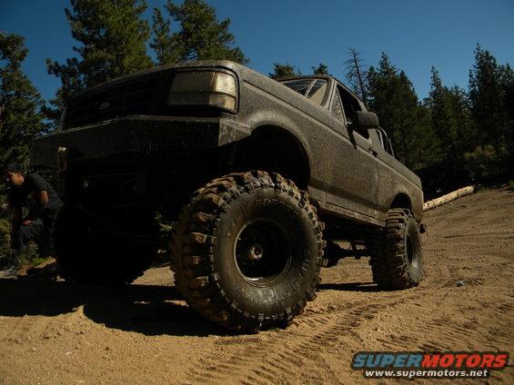 1992 Ford Bronco with large off-road tires on a dirt path, trees in background