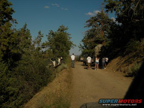 Off-road vehicle tilted on a dirt path with people standing nearby