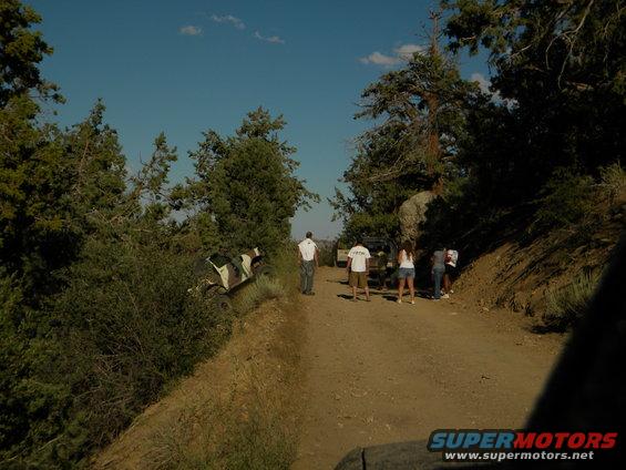 Off-road vehicle on its side on a dirt road with people standing around