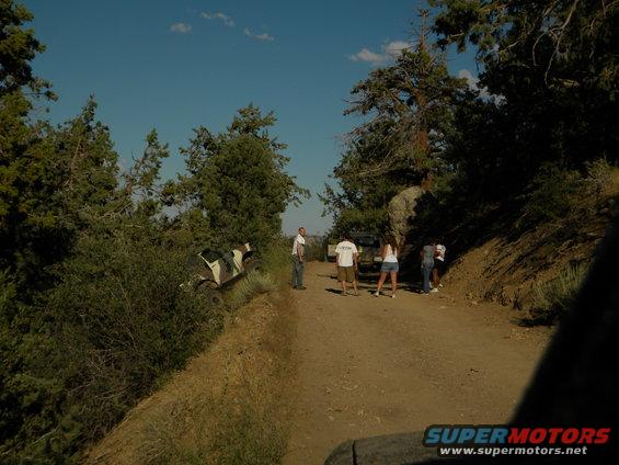Camouflaged off-road vehicle on dirt road with people nearby