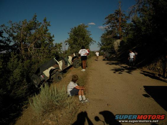 Off-road vehicle tipped on its side on a dirt road with people around