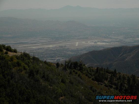 View from a mountain overlooking a valley with an airport and distant mountains