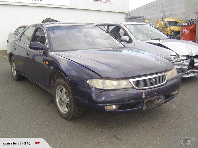 Dark blue sedan parked next to a damaged silver car. The sedan has a grille with a logo and clear headlights