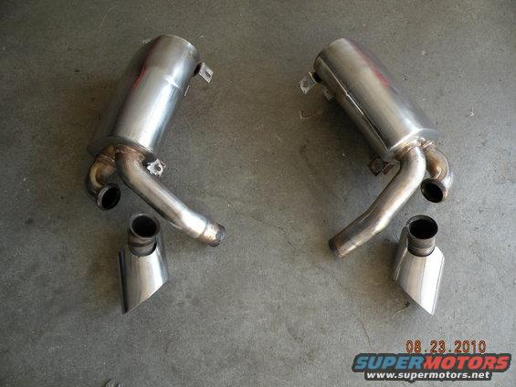 Pair of stainless steel mufflers with exhaust tips on concrete floor. Supermotors.net watermark