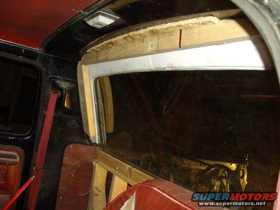 Interior of a vehicle with red seats and a black headliner, showing unfinished wooden framing around a window opening