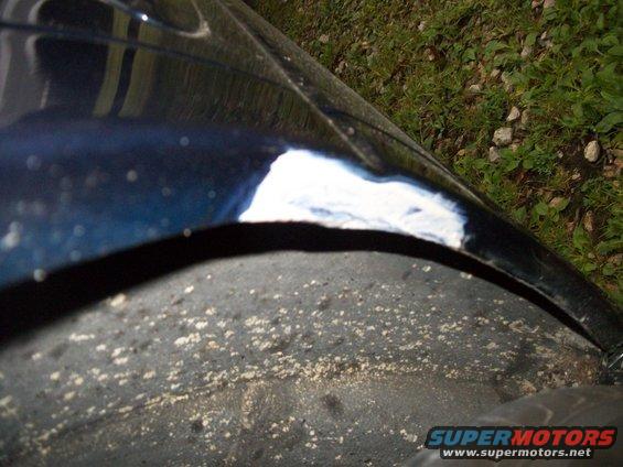 Close-up of a dark blue car fender with a patch of white primer visible near the wheel well